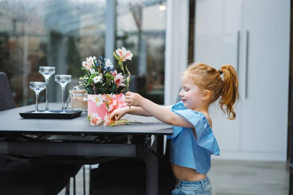 Little girl puts flowers on table — Stock Photo, Image