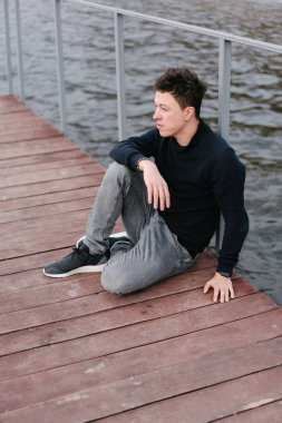 ahşap bir iskele üzerinde oturan genç adam