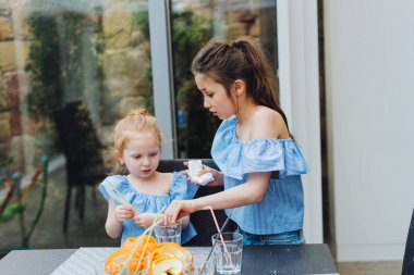 İki kız kardeş mutfakta meyve suyu içiyor.