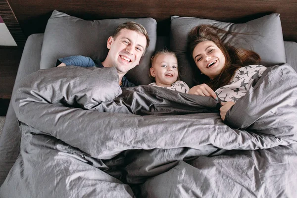 Criança feliz com os pais na cama em casa — Fotografia de Stock