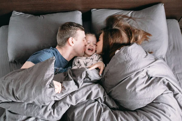 Niño feliz con los padres en la cama en casa —  Fotos de Stock