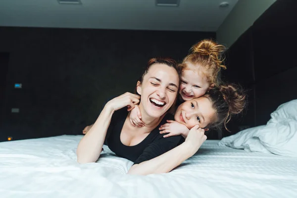 Mom and two daughters have fun on the bed — Stock Photo, Image