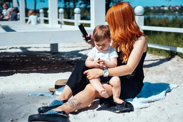 Mamá e hijo descansan en la arena cerca del lago — Foto de Stock