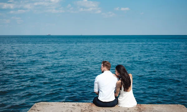 Casal jovem está sentado no cais junto ao mar — Fotografia de Stock
