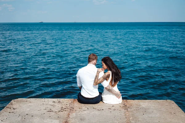 Junges Paar sitzt auf dem Pier am Meer — Stockfoto