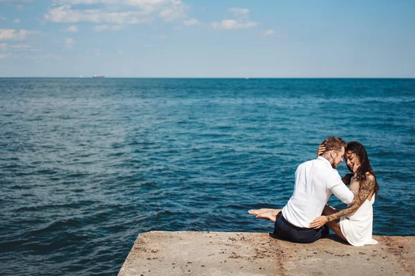 Casal jovem está sentado no cais junto ao mar — Fotografia de Stock