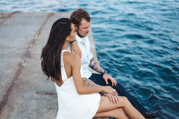 Молода пара сидить на пірсі біля моря — стокове фото