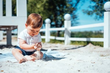 Küçük bebek kumda oturuyor.