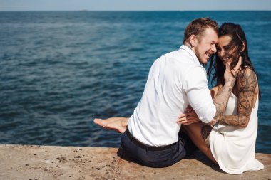 Genç çift deniz kıyısındaki iskelede oturuyor.