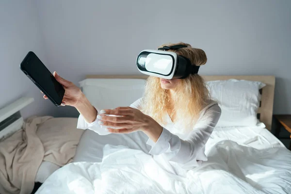 Menina sentada em uma cama com fone de ouvido VR — Fotografia de Stock