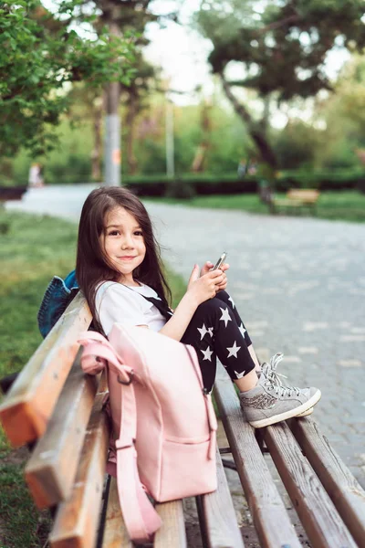 Маленькая девочка со смартфоном сидит на скамейке — стоковое фото