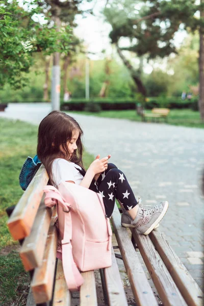 Niña con un teléfono inteligente sentado en un banco — Foto de Stock
