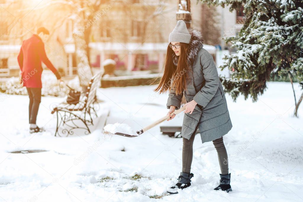Beautiful girl in winter fashion clothes with a shovel