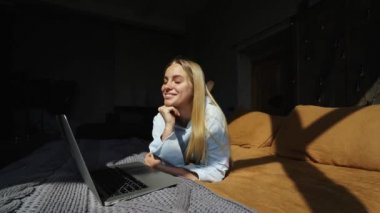 Gülümseyen çekici kadın yatakta laptop kullanarak yatıyor