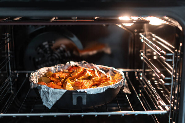 Baked potatoes with carrot and other spices in roasting pan.