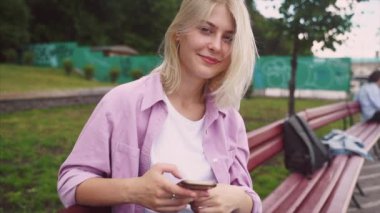 Akıllı telefon kullanan ve bankta oturan genç bir kız.