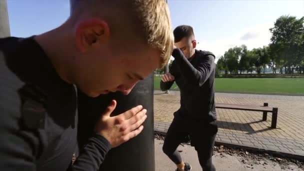 Young boxer hitting a punching bag while friend holding — Stock Video