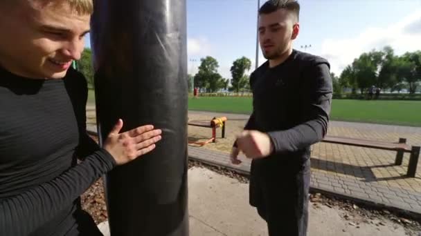 친구를 붙들고 있는 어린 권투 선수가 가방을 때리는 모습 — 비디오