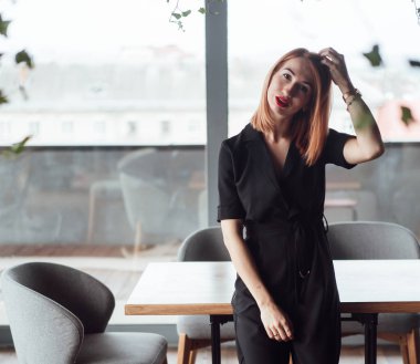 Kamerada poz veren güzel bir kadın büyük bir pencerenin arkasında