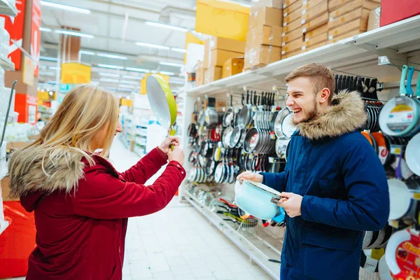 Le gars et la fille choisissent le pot et la poêle dans un supermarché . — Photo