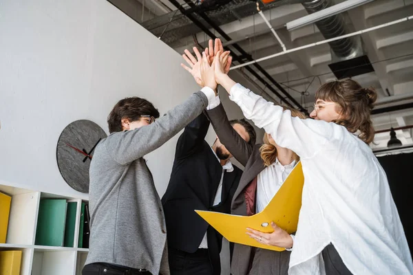 Alegre grupo de jóvenes de pie en la oficina y dando cinco —  Fotos de Stock