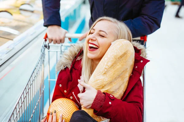 Jeune beau mec monte une fille dans un supermarché dans un chariot — Photo