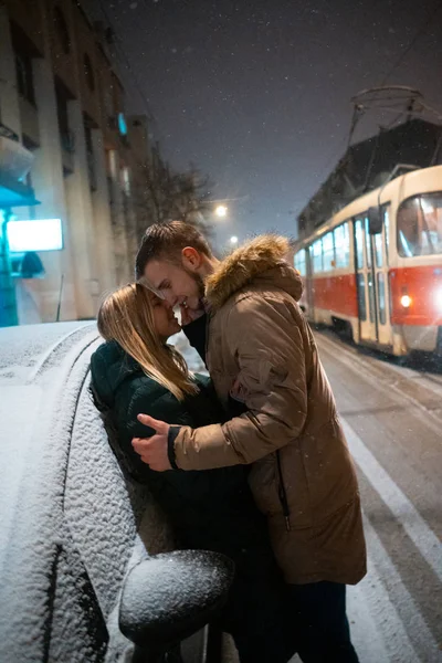 Jovem casal adulto beijando uns aos outros na neve coberta de rua — Fotografia de Stock