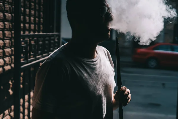 Σιλουέτα του hookah maker φυσάει καπνό στο σκοτάδι. — Φωτογραφία Αρχείου