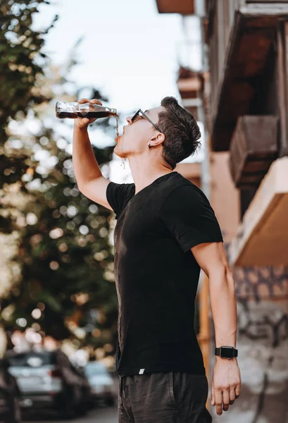 Young attractive hipster man on the street drinks a cool drink on a summer day. — Stock Photo, Image