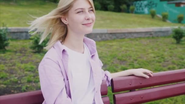 Portrait d'une jolie fille hipster reposant sur un banc en bois du parc — Video