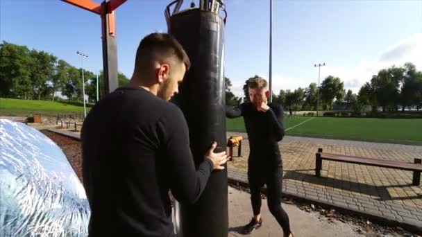 Mladý boxer bít boxovací pytel, zatímco přítel drží — Stock video