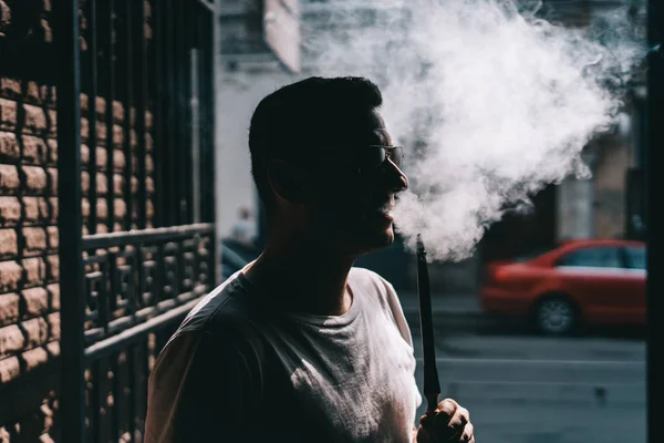 Silueta del fabricante de narguile soplando humo en la oscuridad . — Foto de Stock