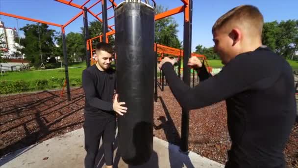 Joven boxeador golpeando un saco de boxeo mientras su amigo sostiene — Vídeos de Stock