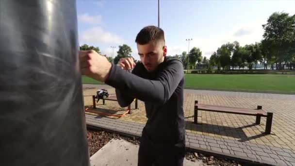 Mladý boxer bít boxovací pytel, zatímco přítel drží — Stock video