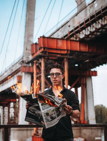 Парень читает горящую газету, на заднем плане мост — стоковое фото