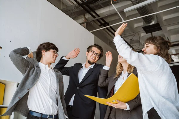 Vrolijke jonge groep mensen staan in het kantoor en geven high five — Stockfoto