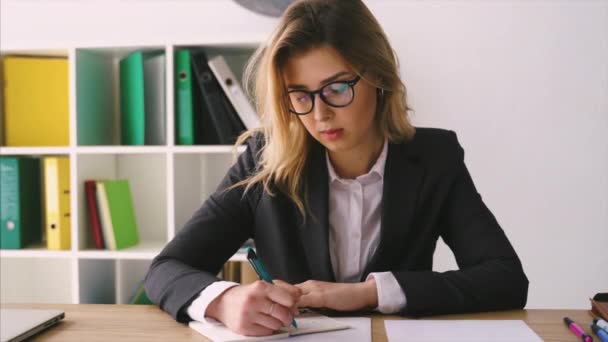 Sonríe mujer de negocios sentada en su escritorio sosteniendo un bolígrafo trabajando con documentos firmar contrato — Vídeos de Stock