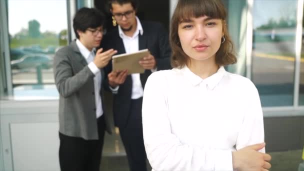 Молодая, красивая женщина позирует перед камерой, на заднем плане два бизнесмена — стоковое видео