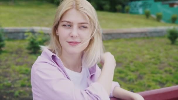 Portrait d'une jolie fille hipster reposant sur un banc en bois du parc — Video