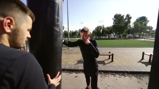 친구를 붙들고 있는 어린 권투 선수가 가방을 때리는 모습 — 비디오