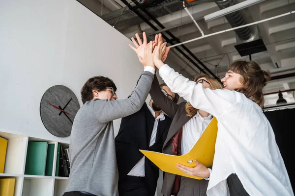 Vrolijke jonge groep mensen staan in het kantoor en geven high five — Stockfoto