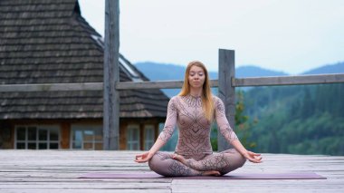 Nilüfer pozisyonunda bir kadın sabahın köründe temiz havada oturuyor..