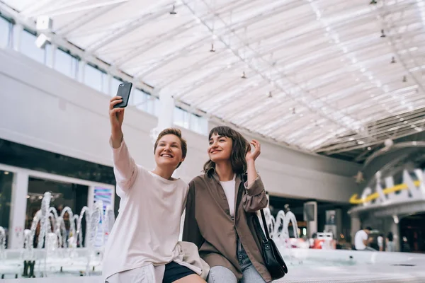 Två flickor tar en selfie i köpcentret, en fontän i bakgrunden — Stockfoto