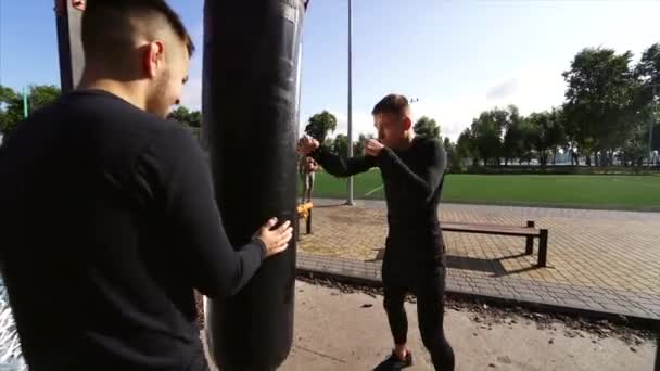 Joven boxeador golpeando un saco de boxeo mientras su amigo sostiene — Vídeos de Stock