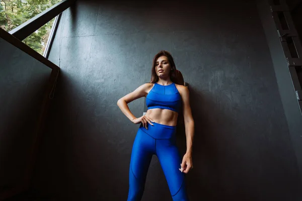 Imagen de la joven deportiva feliz de pie y posando sobre la pared negra. Mirando la cámara. Mujer descansando después de la aptitud . — Foto de Stock