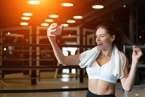 Wanita muda sporty mengambil selfie dengan ponsel untuk jejaring sosial di gym . — Stok Foto