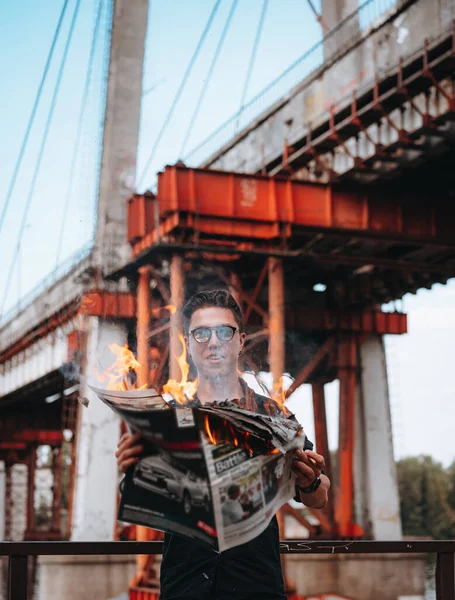 Guy reads a burning newspaper, in the background a bridge — Stock Photo, Image