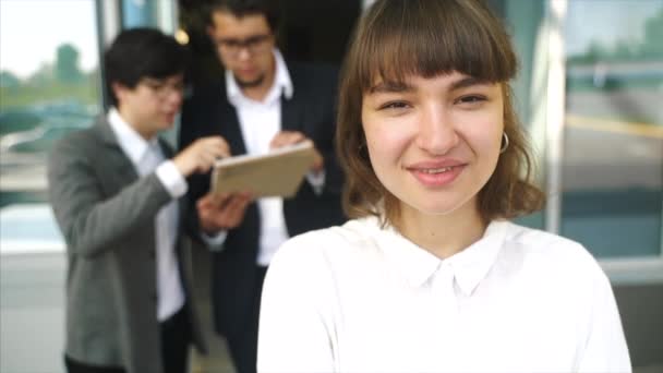 Joven, hermosa mujer posando para la cámara, en el fondo dos hombres de negocios — Vídeo de stock