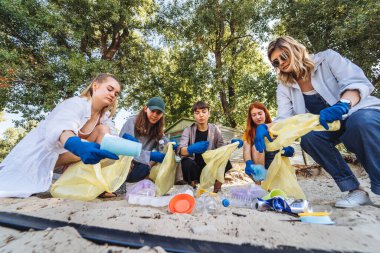 Bir grup aktivist arkadaş plajda plastik atık topluyor. Çevresel koruma.