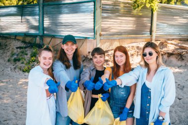 Bir grup aktivist arkadaş plajda plastik atık topluyor. Başparmağınızı kaldırın..